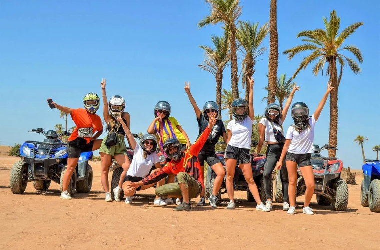 Group of quad bikers wearing helmets celebrating with arms raised in the Palmeraie desert near Marrakech with palm trees and sand dunes