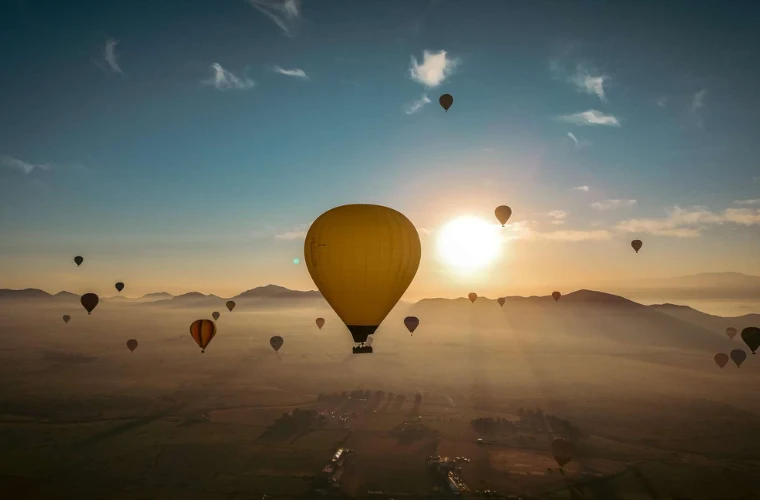 Multiple hot air balloons floating at sunrise over the Atlas Mountains and Marrakech valley with golden morning light and clouds